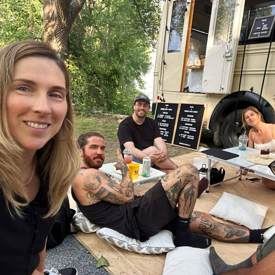 Group of four people enjoying drinks and relaxing on cushions outside the Wonder with Energy bus.